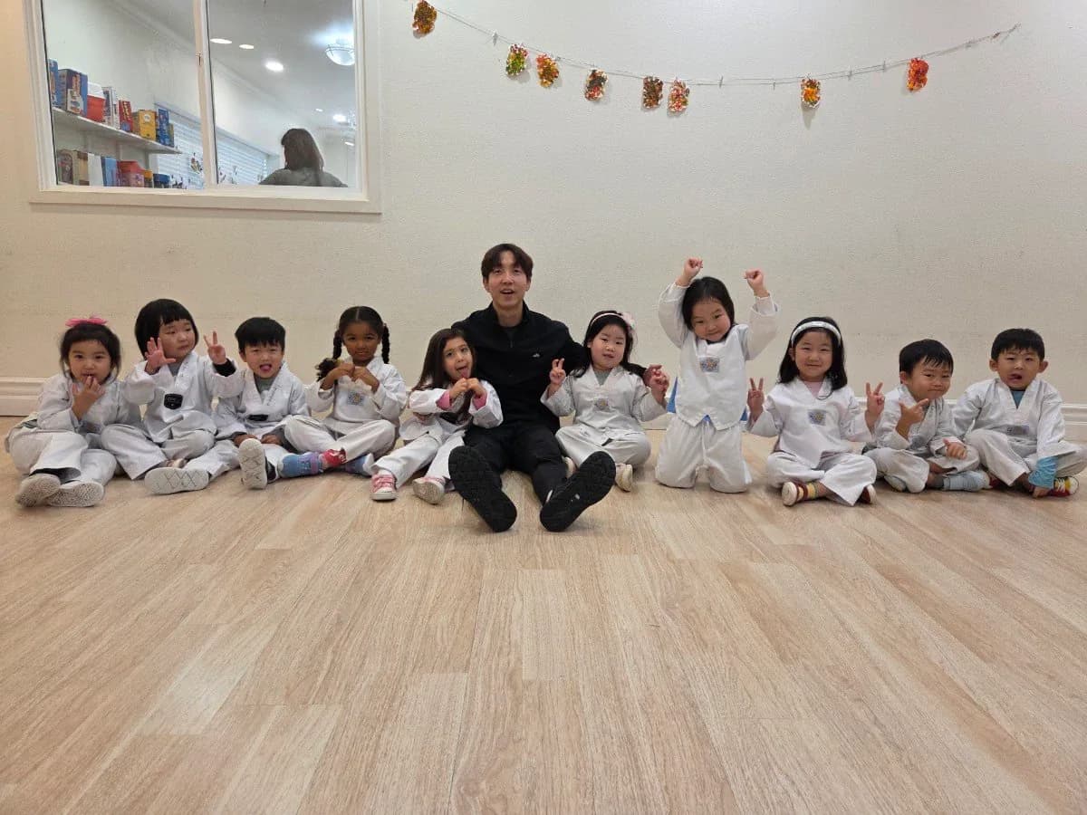 十名身着白色道服的幼童与教练一同坐在训练厅地板上